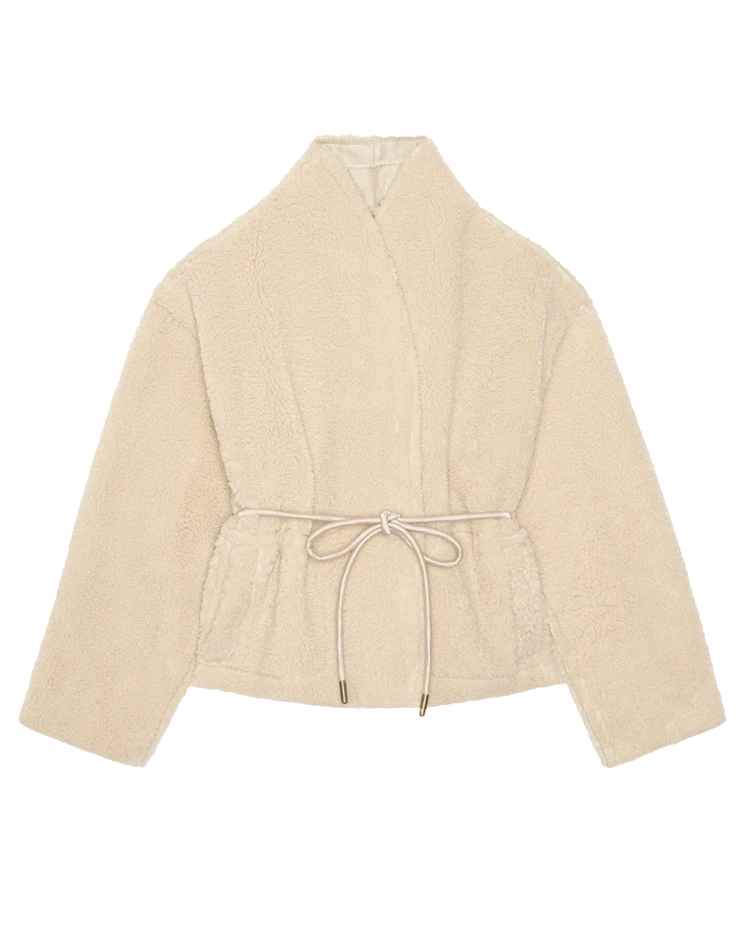 The Reversible Drover Coat by The Great Inc. is a cream-colored, cropped faux shearling coat with wide sleeves, a shawl collar, and a matching fabric belt at the waist, shown against a white background.