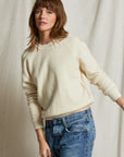 A woman with shoulder-length brown hair wears the Perfectwhitetee Ziggy Reverse LS Sweatshirt and blue jeans, standing before a textured, light-colored fabric backdrop.