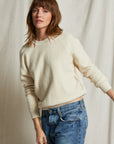 A woman with shoulder-length brown hair wears the Perfectwhitetee Ziggy Reverse LS Sweatshirt and blue jeans, standing before a textured, light-colored fabric backdrop.