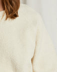 A close-up of someone wearing the Perfectwhitetee Ziggy Reverse LS Sweatshirt in off-white cotton fleece, with only their shoulder, arm, and brown hair visible against a plain background.