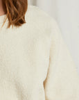 A close-up of someone wearing the Perfectwhitetee Ziggy Reverse LS Sweatshirt in off-white cotton fleece, with only their shoulder, arm, and brown hair visible against a plain background.