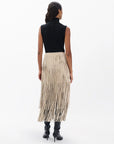 A woman faces away, wearing a sleeveless black top, black knee-high boots, and the Rag & Bone jasmine fringe skirt—a cream-colored skirt with long fringe—set against a plain white background.