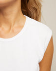 Close-up of a person's neck, shoulder, and part of their face. They are wearing the Perfectwhitetee ELLIE terry banded tank featuring a white ruched waistline. Their light brown wavy hair is partially visible against a neutral, blurred background.