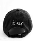 The Kerri Rosenthal Baseball Hat Heart Patch, shown from the back on a white background, features "loved" and a heart embroidered in white cursive above the adjustable strap—a stylish take on popular black baseball caps.