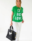 Kerri Rosenthal KR Imperfect Heart Tote with leather charm, styled with green graphic tee and white pants.