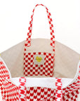 The KR Heart in Check Tote by Kerri Rosenthal is a white cotton canvas bag with red geometric patterns, yellow corner accents, and an inner label reading “KARLA EARNSHAW,” shown against a plain white background.