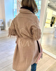 A person models the Kerri Rosenthal Cali Fringe Cardigan Coat indoors, facing away in a bright room with large windows, white walls, wooden floors, and vibrant displays of artwork and clothing.
