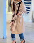 A person wearing the Kerri Rosenthal Cali Fringe Cardigan Coat, cuffed blue jeans, a multi-colored scarf partially covering their face, and leopard print shoes stands indoors near a blue pillar.