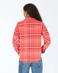 A person with long curly hair, wearing the Kerri Rosenthal Pia Western Flannel in red and pink and blue jeans, stands facing away from the camera against a plain white background.