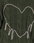 A close-up of the dark green Kerri Rosenthal Shawl Collar Helen Cardigan, featuring a drippy heart outlined in a multicolored braided cord, with the bottom of the heart appearing to melt downward.