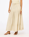 A woman models the Kerri Rosenthal Vacance Pintuck Skirt, featuring tiered lace trim, paired with a sleeveless beige top and brown strappy sandals. She stands against a white background with her face not shown.