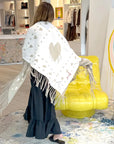 Kerri Rosenthal Imperfect Heart Poncho in black, styled in a bright boutique with yellow accent chair.