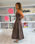 A woman in the Kerri Rosenthal KR Tank Dress stands sideways in a brightly lit art studio, with abstract paintings, decorative masks, and an electric guitar displayed on white shelves behind her.