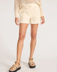 A person stands against a plain white background wearing BROCHU WALKER’s KAIA EMBROIDERED SHORT, crafted from Italian fabric, paired with a cream knit sweater and beige platform sandals. The image is cropped above the shoulders.