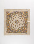 The Hachiko Scarf by Kujten is a beige square accessory made from printed jersey with frayed edges, showcasing a detailed paisley and floral pattern in yellow, brown, and black.