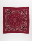 The Hachiko Scarf by BCS Group is a square maroon bandana in printed cashmere, featuring white and black paisley details with subtle frayed edges, shown flat on a white background.