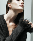 A person with long straight hair wears the Le Superbe Fresange Cardigan, posing with their head tilted back and chin raised. Lighting highlights their smooth skin and the cardigan’s fuzzy knit sleeve detail.