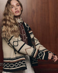 The Bear Lodge Cardigan by The Great Inc. in a cozy, rustic style, shown against a wood-planked wall.