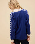 A person with long blonde hair faces away, wearing the DayDreamer Los Angeles Stars Rugby top—featuring white cuffs, collar, and star-striped sleeves—against a plain beige background.