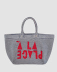 The Clare Vivier La Plage Tote is a large cotton terry cloth bag with two handles, featuring bold red “A LA PLAGE” text and shapes over black-and-white horizontal stripes on the front for a striking beach look.