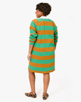 A person wearing the Clare Vivier Le Rugby Dress, featuring wide green and orange stripes on heavyweight cotton, is seen from behind against a plain white background. They pair it with leopard print shoes and have curly hair.