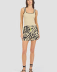 A woman in a beige square-neck tank top, Le Superbe BoHo Rhapsody Beach Boxer with neon yellow drawstring, and black strappy sandals stands against a light gray background.