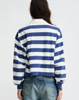 A woman with brown hair wears the Denimist Rugby LS Tee in blue ecru stripe and frayed denim shorts, facing away against a plain white background.