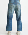Back view of a person wearing Denimist HAISLEY SLOUCH BF JEAN in faded blue with wide legs and frayed hems, paired with white sneakers. Made from premium denim, shown against a plain white background.