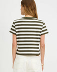 A woman with long brown hair faces away, wearing the Denimist STRIPED BABY T—a short-sleeve olive green and white crewneck tee—paired with high-waisted white jeans, set against a plain white background.