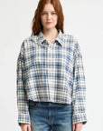A person with long, reddish-brown hair wears the Denimist CROPPED BUTTON FRONT SHIRT in blue and white plaid with a boxy fit, paired with blue jeans, standing against a plain white background.
