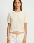 A woman models the Denimist SHORT SLEEVE CABLE CREWNECK in cream, paired with high-waisted white jeans, standing against a plain white background and looking at the camera.