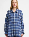 A person with long, light brown hair wears the Denimist BUTTON FRONT SHIRT in blue/ecru plaid, styled with matching plaid pants, standing against a plain white background.