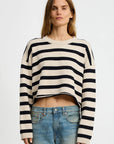 A person with long hair wears the Denimist CROPPED STRIPE SWEATER featuring black horizontal stripes, paired with blue jeans, and stands against a plain white background.