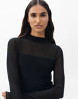 A woman with long dark hair models the Rag & Bone luca dbl layer mix media mockneck long-sleeve top in black, standing confidently against a plain white background.