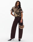 A woman stands against a plain background wearing the Rag & Bone lucy sequin tee, wide-leg brown pants, black heeled shoes, and holding a small round beige fur handbag—an ideal look for party season.