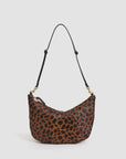 The F25- Lune by Clare Vivier is a curved brown shoulder bag in black leopard-print hair-on leather, featuring a zipper closure and an adjustable black strap with gold hardware.
