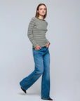A woman stands with her hands in her jeans pockets, wearing the Majestic Filatures Organic Cotton Stripe L/S Crewneck and wide-leg blue jeans against a plain light gray background.