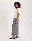 A person with curly hair wears a loose, short-sleeve Naomi Tee Shirt by Ines De LA Fressange and a long, black-and-white striped skirt, standing sideways against a plain light background, finished with black sandals.