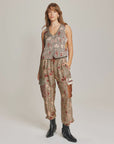 A person stands against a plain background wearing Me369's Gianna Cargo Pants, featuring a high-waisted Rodeo print and "Gou" patch, paired with a sleeveless patterned top and black ankle boots, with one hand in their pocket.