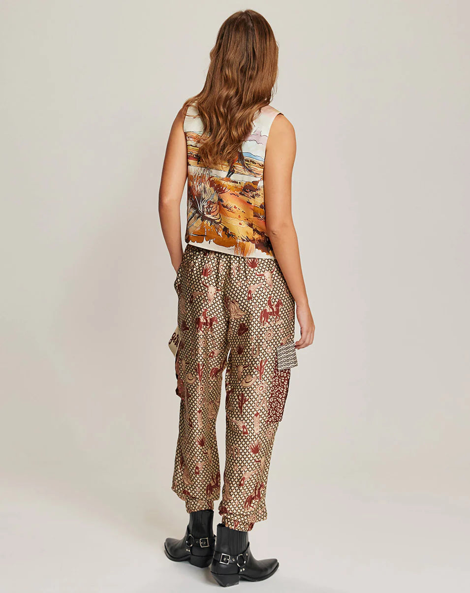 A woman with wavy brown hair, seen from the back, wears Me369's Gianna Cargo Pants with elastic waist, styled with a sleeveless scenic top and black ankle boots, standing against a plain light background.