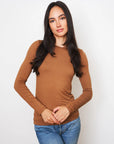 A woman with long dark hair wears a Majestic Filatures Soft Touch L/S Crewneck T-Shirt in brown and blue jeans, standing against a plain white background and looking at the camera with a relaxed expression.