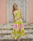 A person stands on stone steps in front of a textured wooden door and pink wall, wearing the vibrant Fallon Skirt by Hunter Bell NYC with custom print patterns in green, pink, and white, creating a summery and stylish atmosphere.