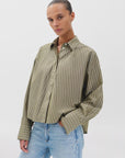 A woman wears the Rag & Bone martha poplin striped shirt in olive green with white vertical stripes, styled with light blue jeans, standing against a plain white background.