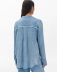 A person with long dark hair is seen from behind, wearing the Rag & Bone miramar slink long sleeve lounge shirt in a light blue denim print, paired with matching pants, set against a plain white background.