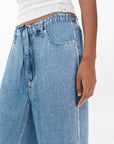 A person wears Rag & Bone's miramar slink lounge pant in blue with a white ribbed tank top, shown midsection to thigh against a plain white background.