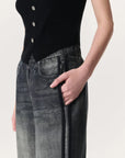 A person wears Rag & Bone's Miramar Wide Leg Track Pant and a sleeveless black buttoned top, standing with one hand in their pocket against a light background.