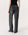 A person stands facing away from the camera, wearing a black sleeveless top and Rag & Bone Miramar Wide Leg Track Pants in faded black denim with back pockets against a plain light background.