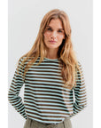 A person with long hair wearing Kule's The Modern Long, a lightweight Portuguese cotton striped long-sleeve shirt, stands against a plain background.