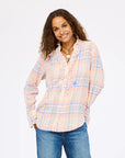 A woman with wavy brown hair smiles, wearing the Kerri Rosenthal Molly Shirt with ruffle front details and blue jeans, standing against a plain white background.