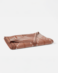 The Morelia Beach Towel by Coyuchi Inc, featuring a white and black abstract line pattern on a brown velour terry weave, is displayed on a plain white background.